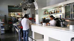 A modern bar area with a counter, shelves with bottles, and a person preparing drinks. - Biancoreroma B&B (Rome)