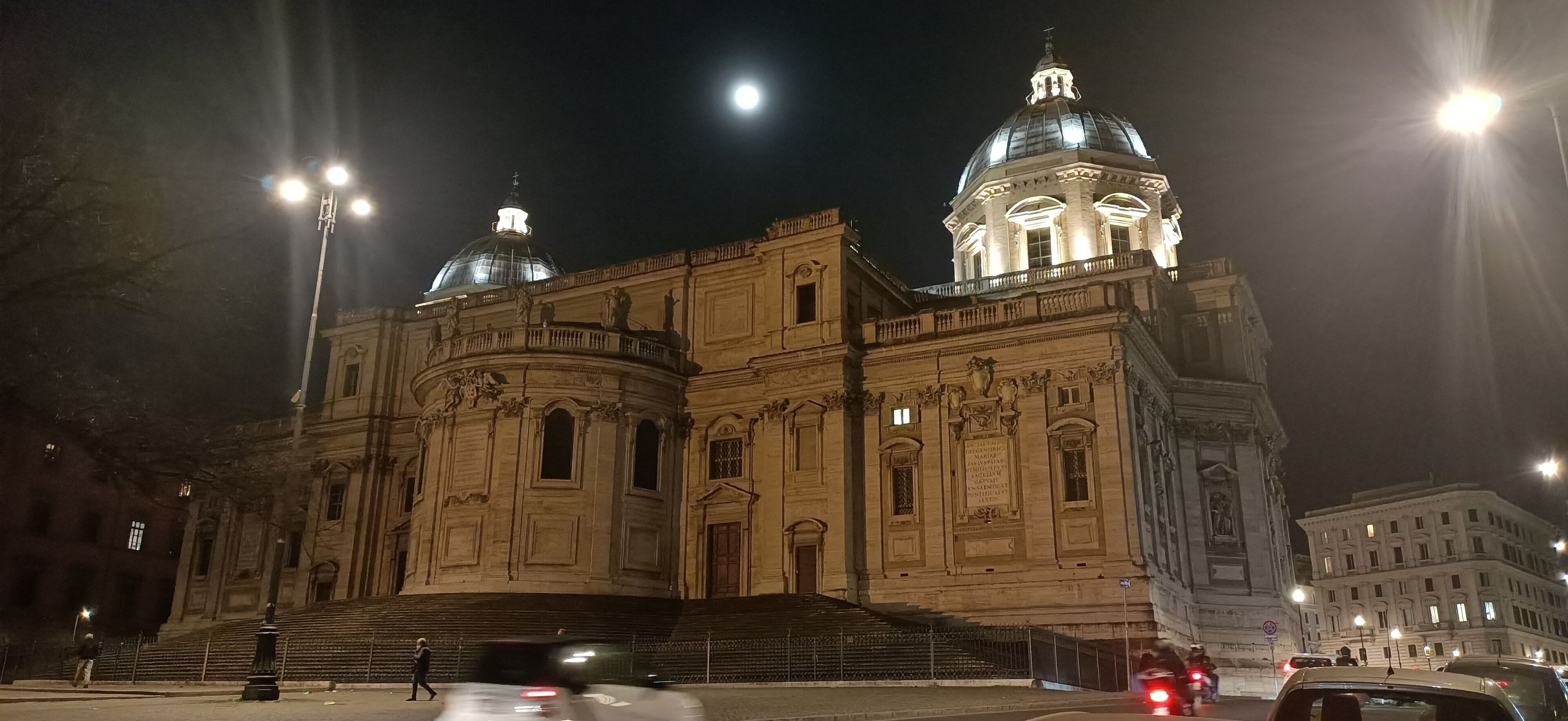 A large, historic building with a prominent dome and classical architecture, featuring a grand staircase leading to the entrance.