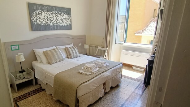A hotel room with a bed, bedside tables, a lamp, a radiator, and a window with curtains. - Biancoreroma B&B (Rome)