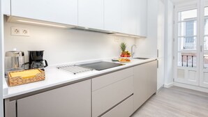 Une cuisine moderne avec des meubles blancs, un plan de travail noir et une cuisinière encastrée. On peut voir un panier de fruits contenant des ananas et des oranges sur le plan de travail.