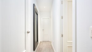 Un couloir étroit aux murs blancs et au plancher en bois, qui mène à une porte blanche au bout.