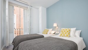 Une chambre avec deux lits, un balcon et une lampe fixée au mur.