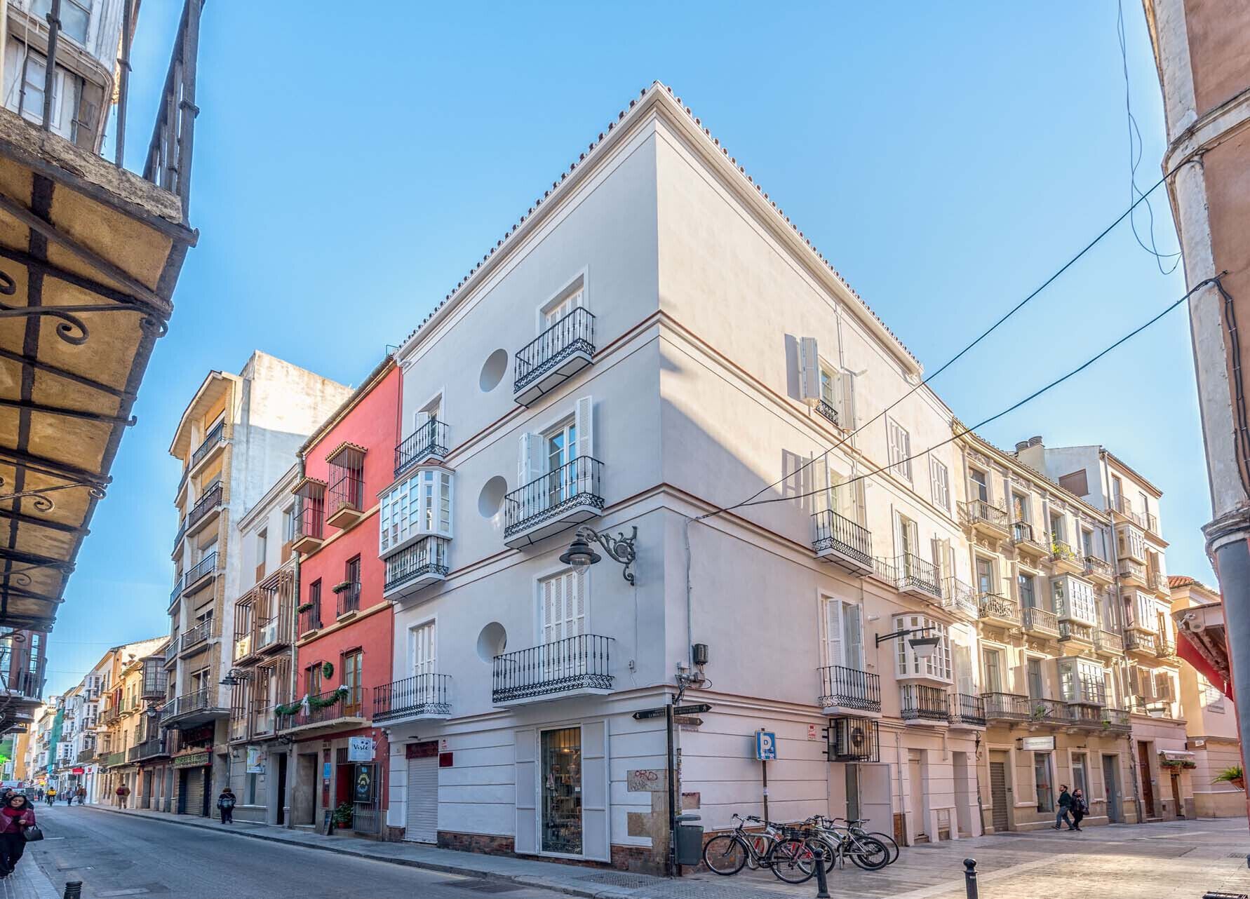 A multi-story building with balconies, a street in front, and a clear sky.