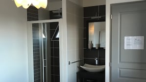A hotel room with a bed, a bathroom with a shower, a sink, and a door. - Les Algues du Grau (Agde)
