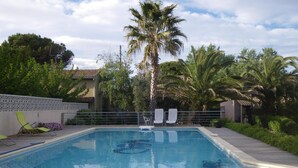 A rectangular swimming pool with a tiled deck, surrounded by palm trees and a fence. - Les Algues du Grau (Agde)