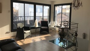 A spacious living room with large windows, a glass coffee table, a black sofa, and a white chair. - Les Algues du Grau (Agde)
