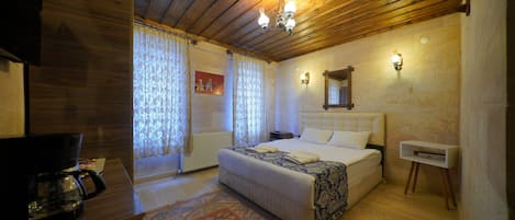 A bedroom with a wooden ceiling, a bed with a white headboard, a bedside table, a nightstand, a wall-mounted lamp, and a patterned rug.