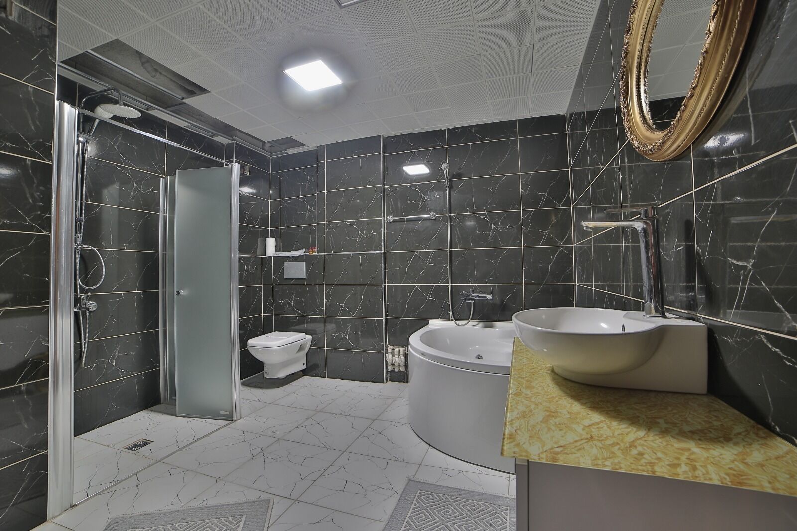 A modern bathroom with a glass-enclosed shower, a toilet, a bathtub, and a sink with a large mirror.