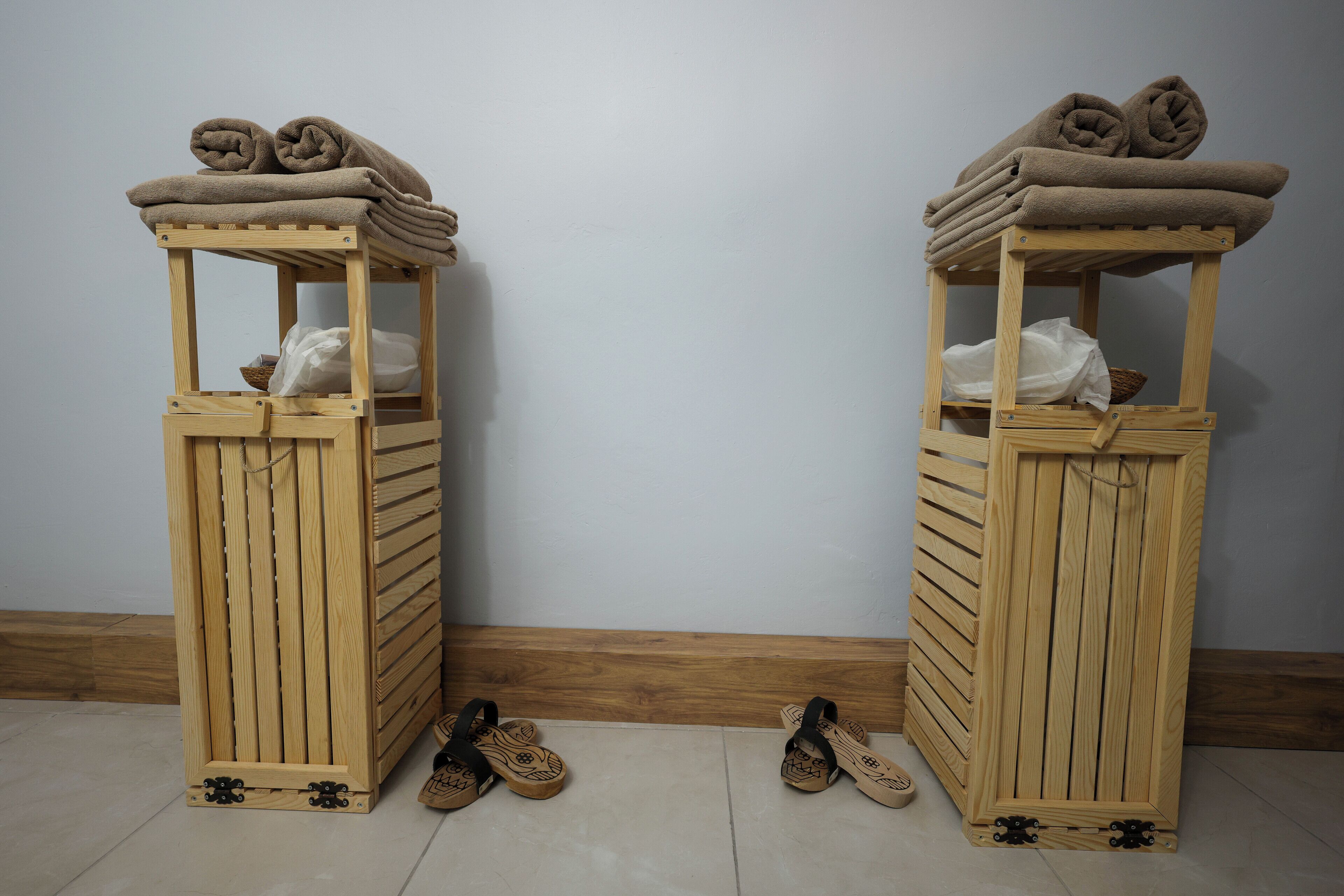 Two wooden shoe racks with folded towels on top and a pair of sandals in front.