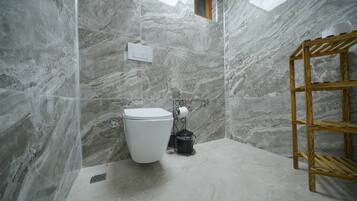 Un baño con pared de mármol, inodoro blanco, repisa de madera y tragaluz.