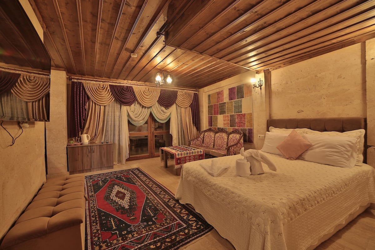 A traditional room with a bed, a bench, a patterned rug, and a wooden ceiling.