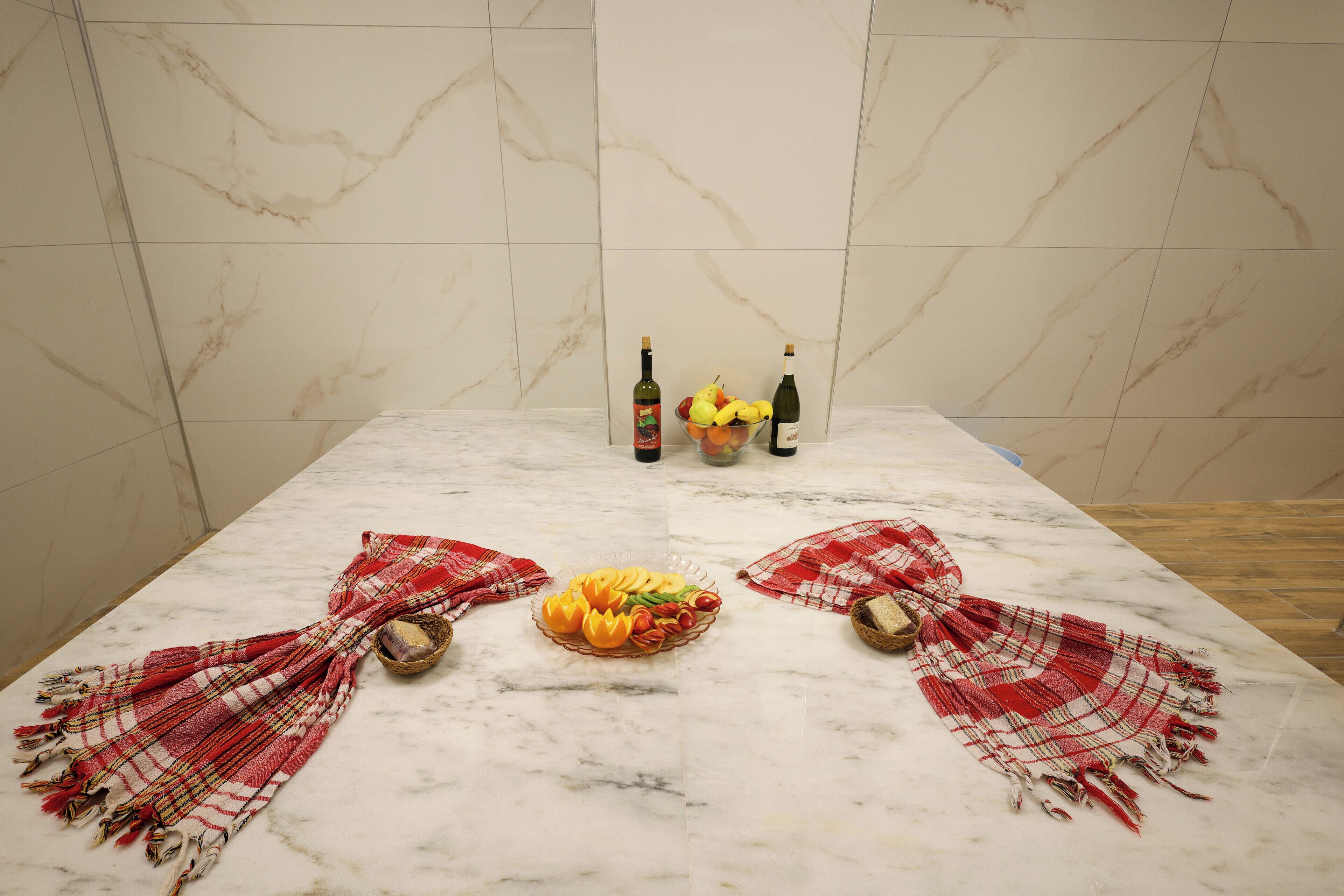Una mesa con loseta de mármol, un frutero, botellas y un mantel a cuadros.