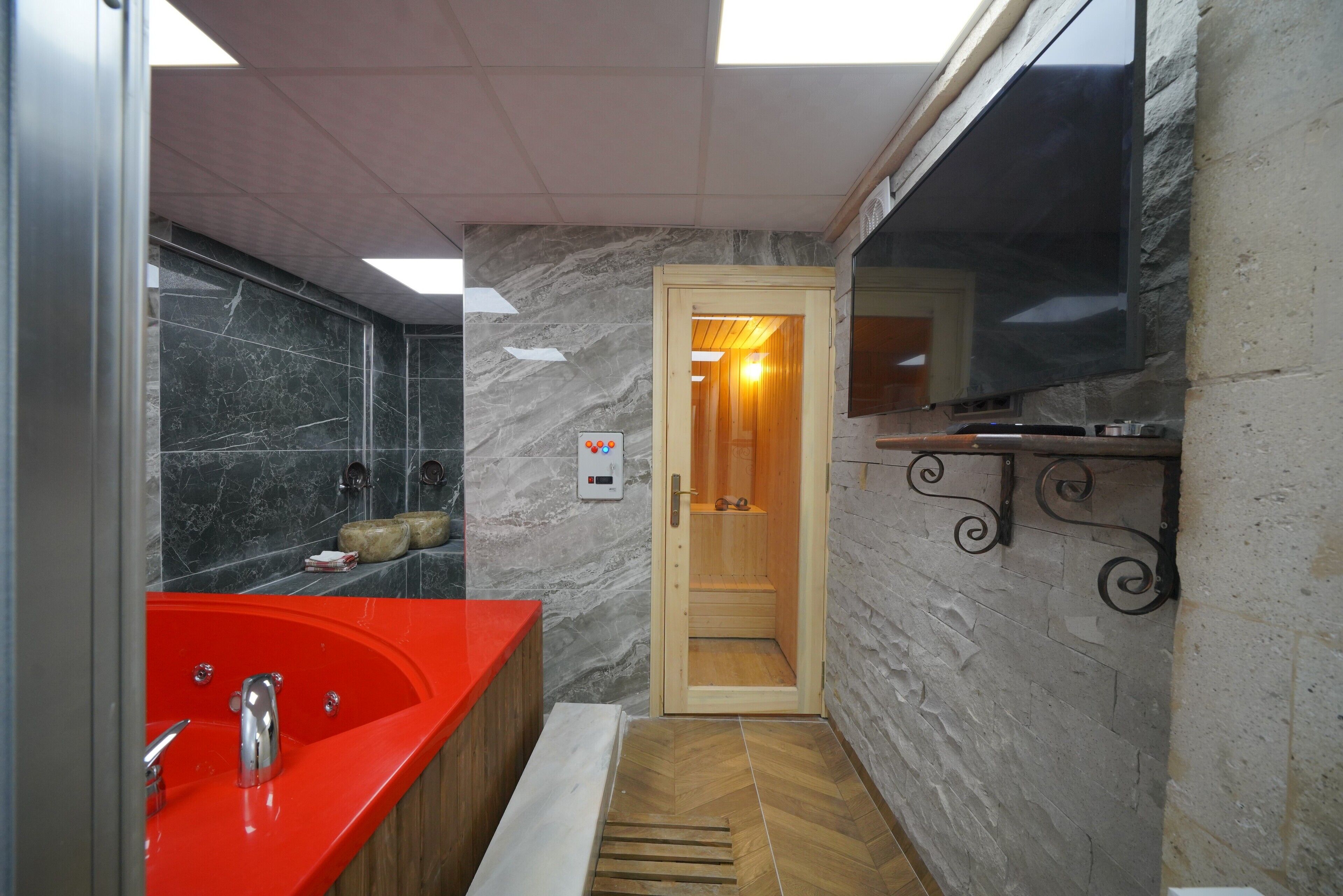 Un baño moderno con un lavabo rojo, una puerta de madera que da a una zona de ducha y una pared de mármol.