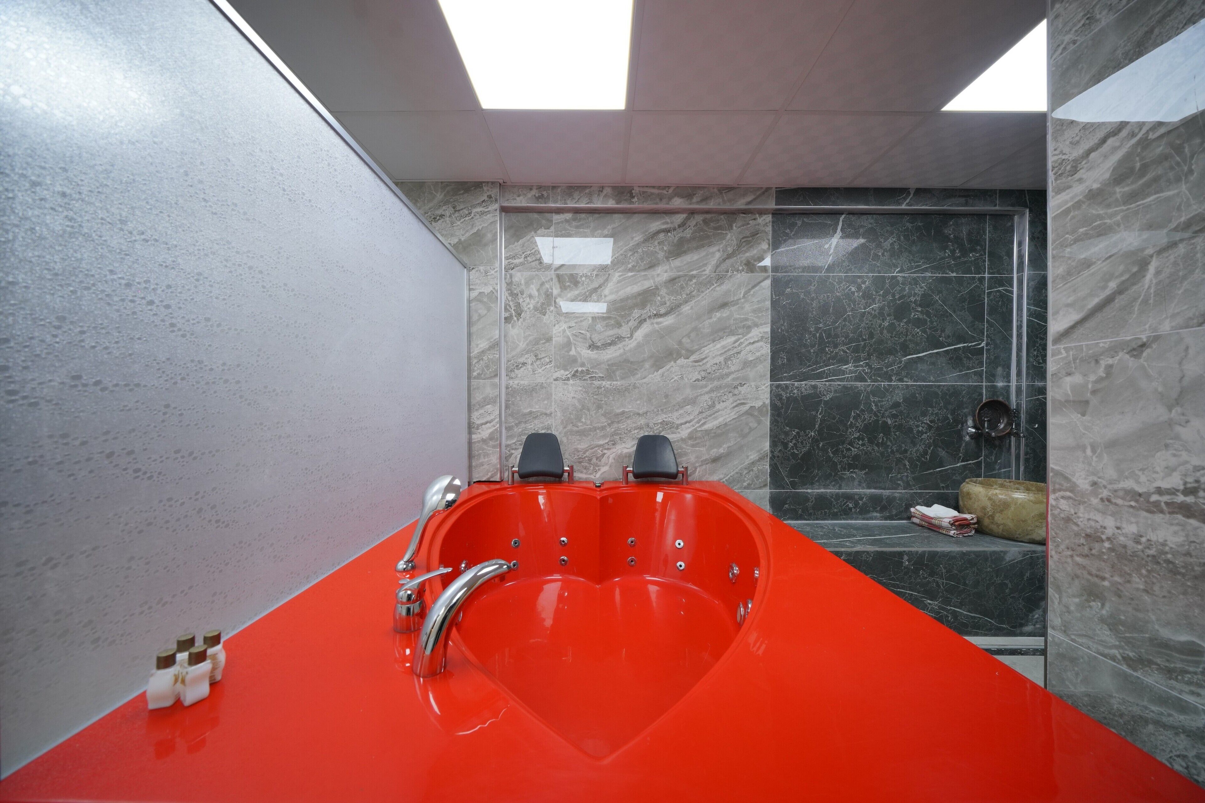 A modern bathroom with a heart-shaped bathtub, a glass shower enclosure, and marble walls.