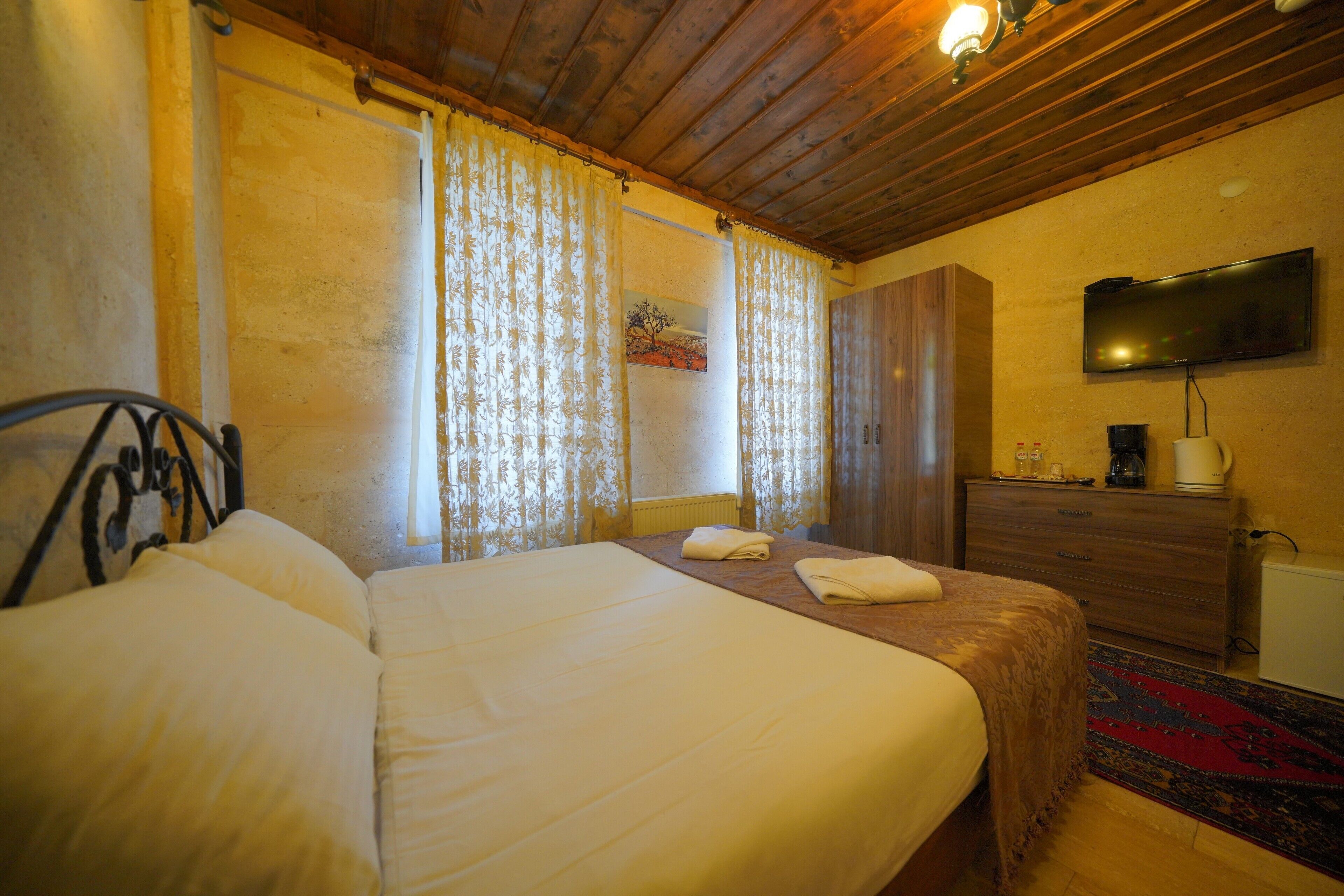 A hotel room with a large bed, wooden ceiling, curtains, a television, a dresser, and a radiator.