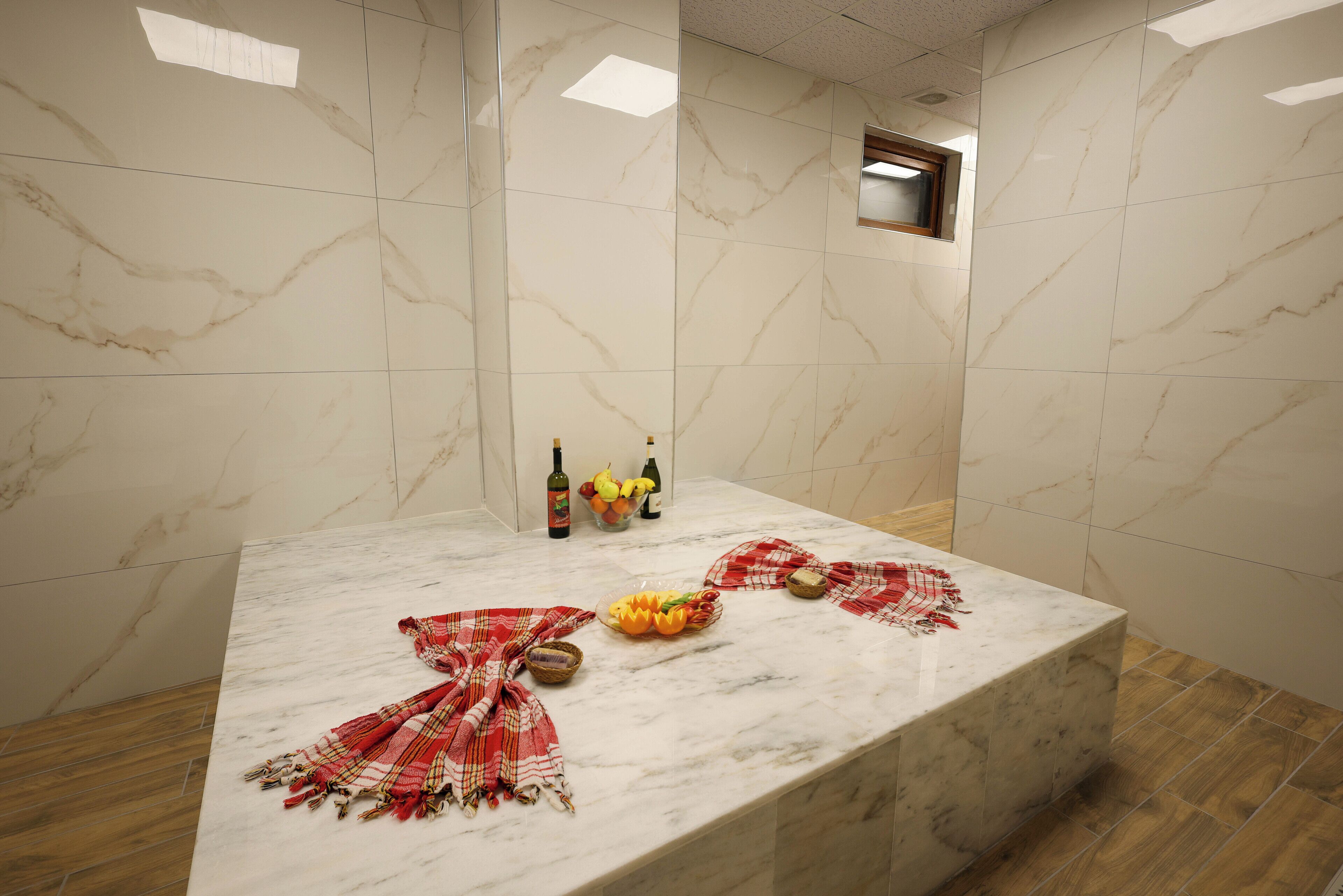 A marble-tiled bathroom with a sink, bottles, and a bowl of fruit.