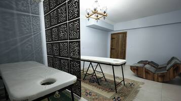A room with a massage table, patterned wall panels, a wooden door, and a unique seating area.