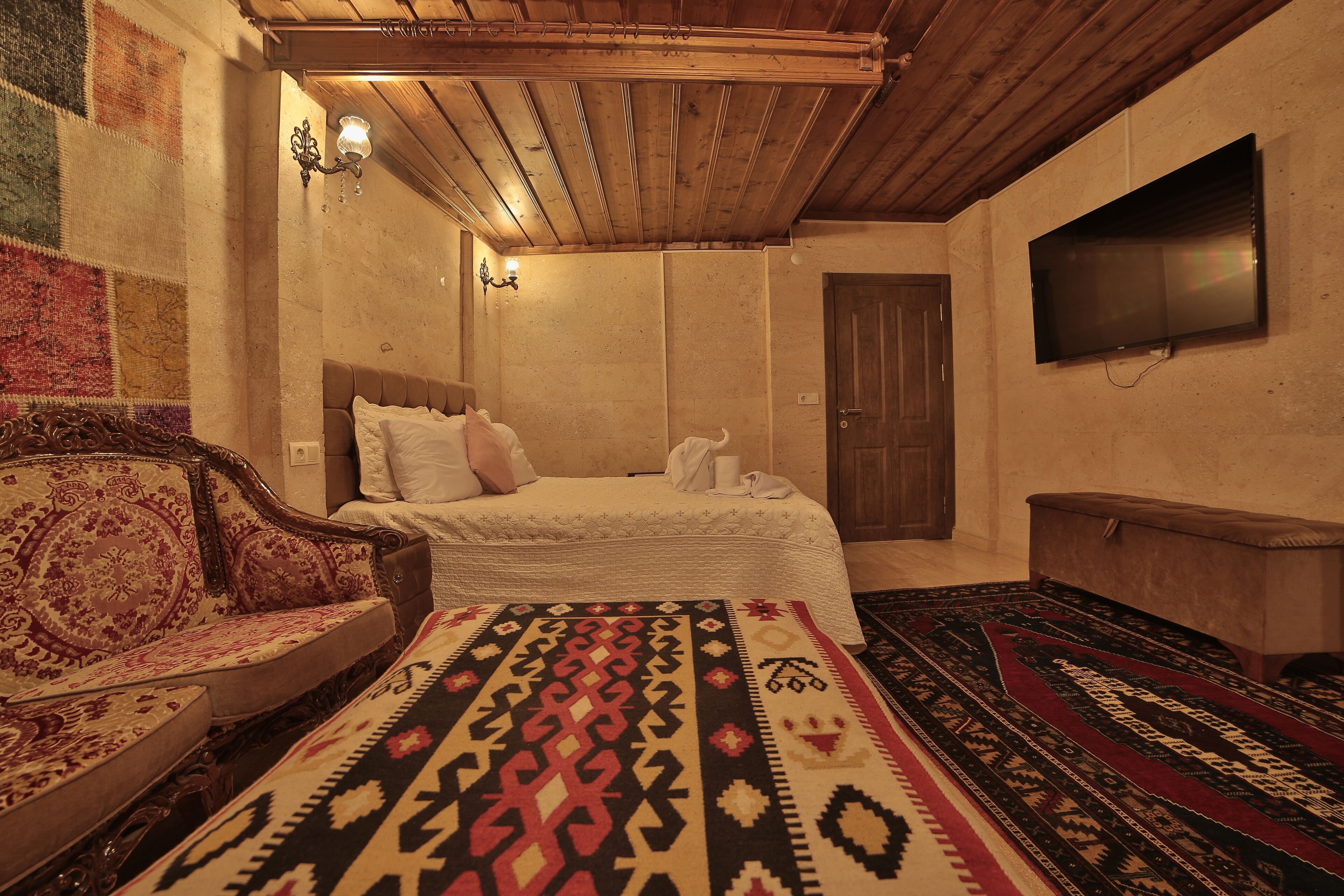A room with a bed, a sofa, a television, and a patterned rug.