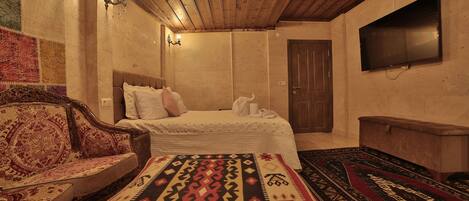 A room with a bed, a sofa, a television, and a patterned rug.