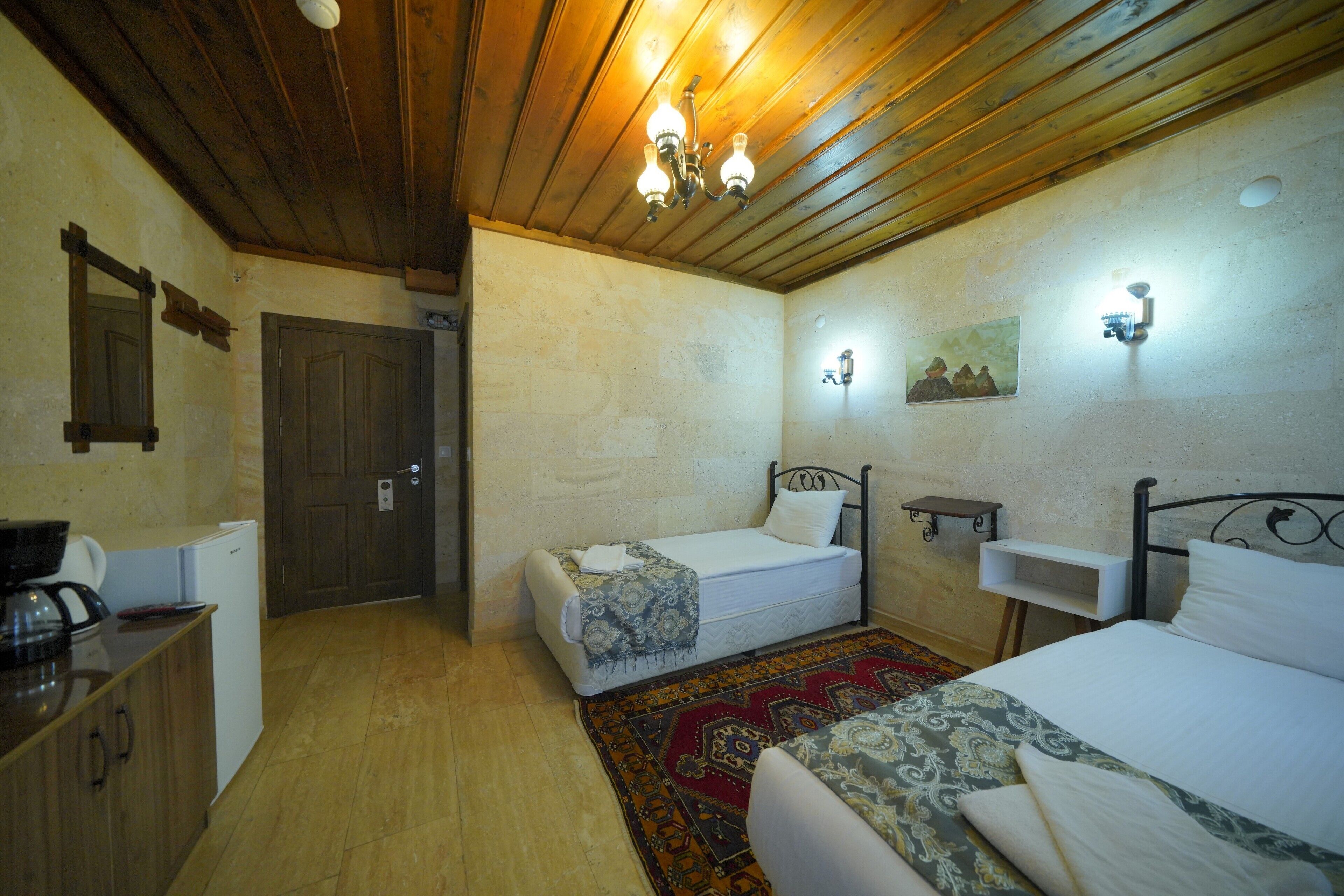 A room with two beds, a wooden ceiling, a small kitchenette, and a door.
