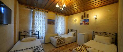 A room with two single beds, a wooden ceiling, a flat-screen TV, and a painting on the wall.
