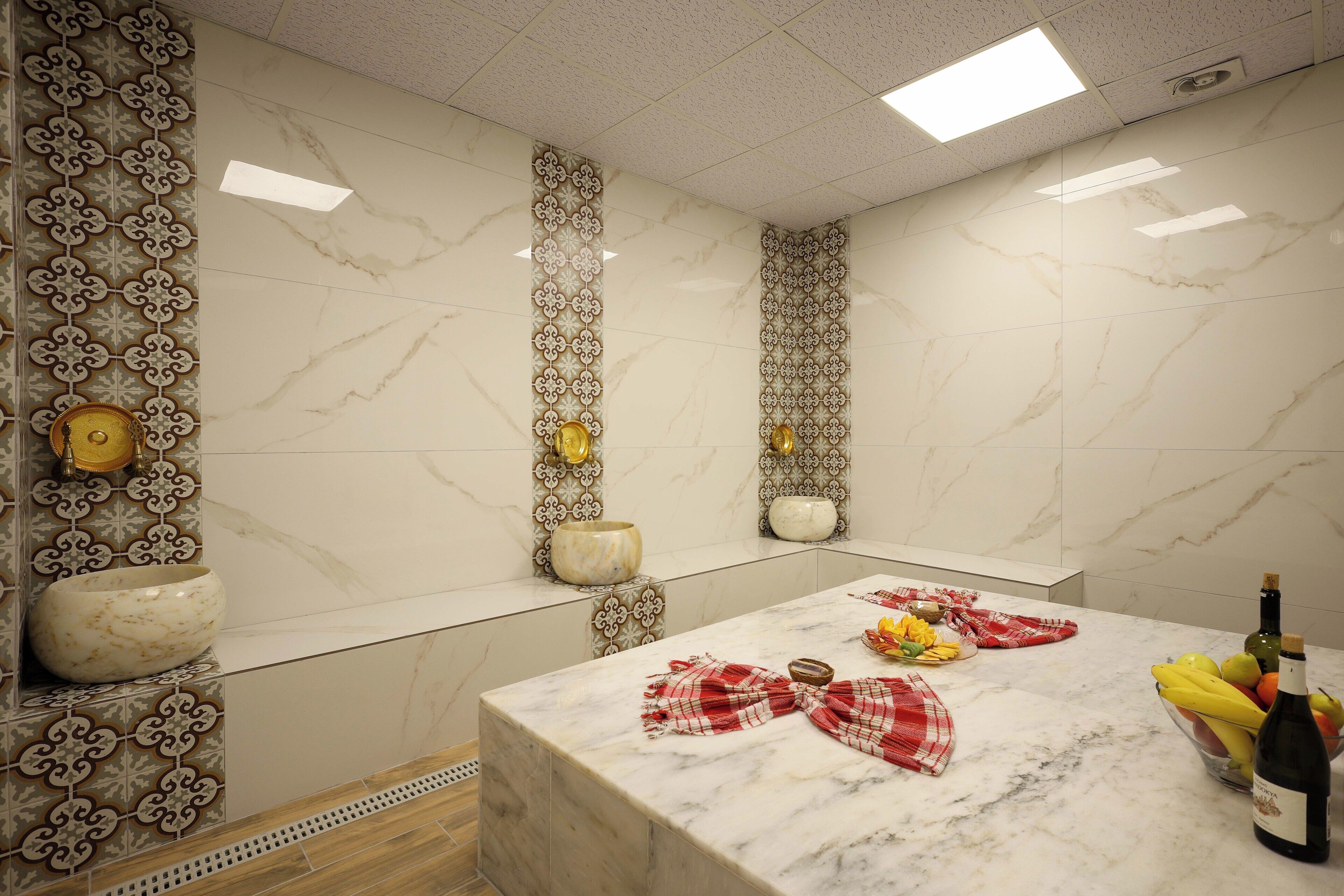 A kitchen with a marble countertop, decorative wall tiles, and a bowl of fruit.