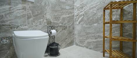 A bathroom with a toilet, marble walls, a wooden shelf, and a toilet paper holder.