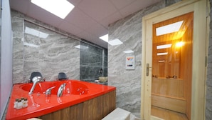 Un baño moderno con un lavamanos rojo, dos grifos, una puerta de madera y una pared de mármol.