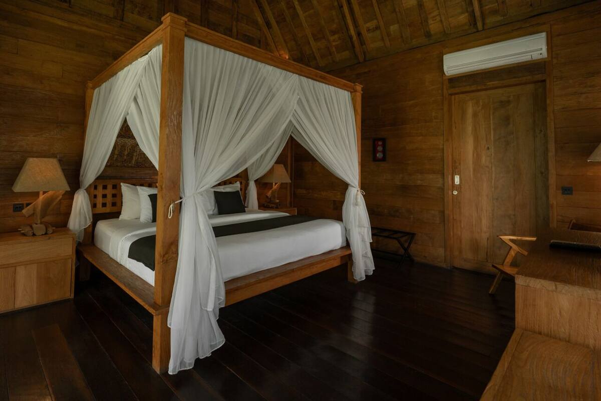 A four-poster bed with white drapes, a wooden headboard, and a bedside table with a lamp.