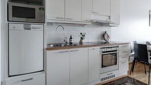Una cucina moderna con mobili bianchi, un forno a microonde, un forno integrato, un lavello e un'area pranzo con una sedia nera.