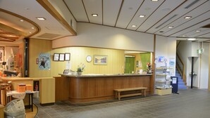 A reception area with a wooden counter, a clock, framed pictures, and a green door. - Miyajima MorinoYado Inn (Hatsukaichi)