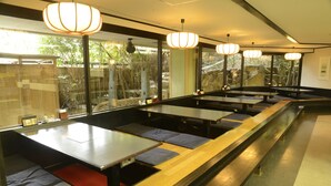 A restaurant with long communal tables and benches, large windows with a view of greenery, and hanging pendant lights. - Miyajima MorinoYado Inn (Hatsukaichi)