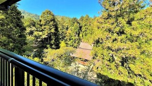 A view from a balcony overlooking a forested area with a building in the background. - Miyajima MorinoYado Inn (Hatsukaichi)