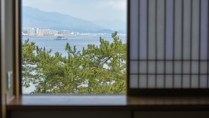 A view through a window with a cityscape, including buildings and a body of water, with mountains in the background. - Miyajima MorinoYado Inn (Hatsukaichi)