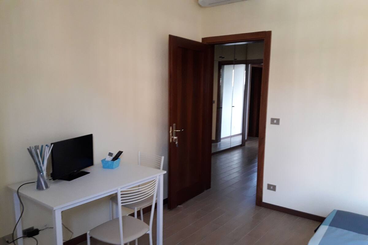 A room with a white desk, a chair, a television, and a door leading to another room.