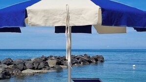Una playa con dos sillas azules para tomar el sol y una sombrilla azul y blanca.