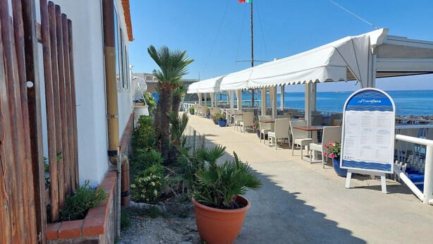Un restaurante frente al mar con terraza, un cartel de menú y vistas al océano.
