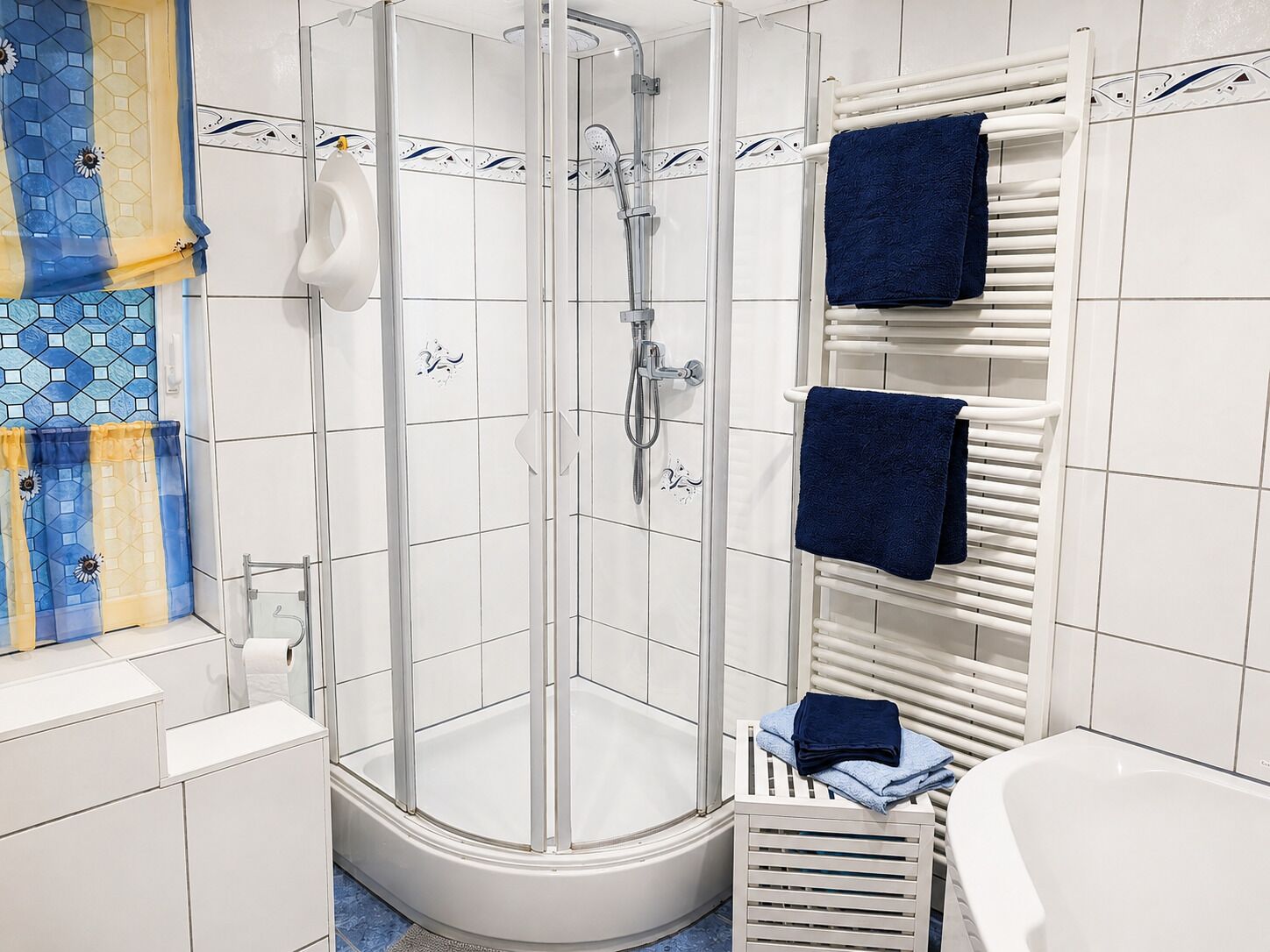Une salle de bain moderne avec une douche à parois de verre, des murs recouverts de carreaux blancs, une baignoire blanche et un porte-serviettes avec deux serviettes.
