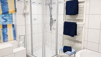 Ein modernes Badezimmer mit einer gläsernen Duschkabine, weißen Fliesenwänden, einer weißen Badewanne und einem Handtuchhalter mit zwei Handtüchern.