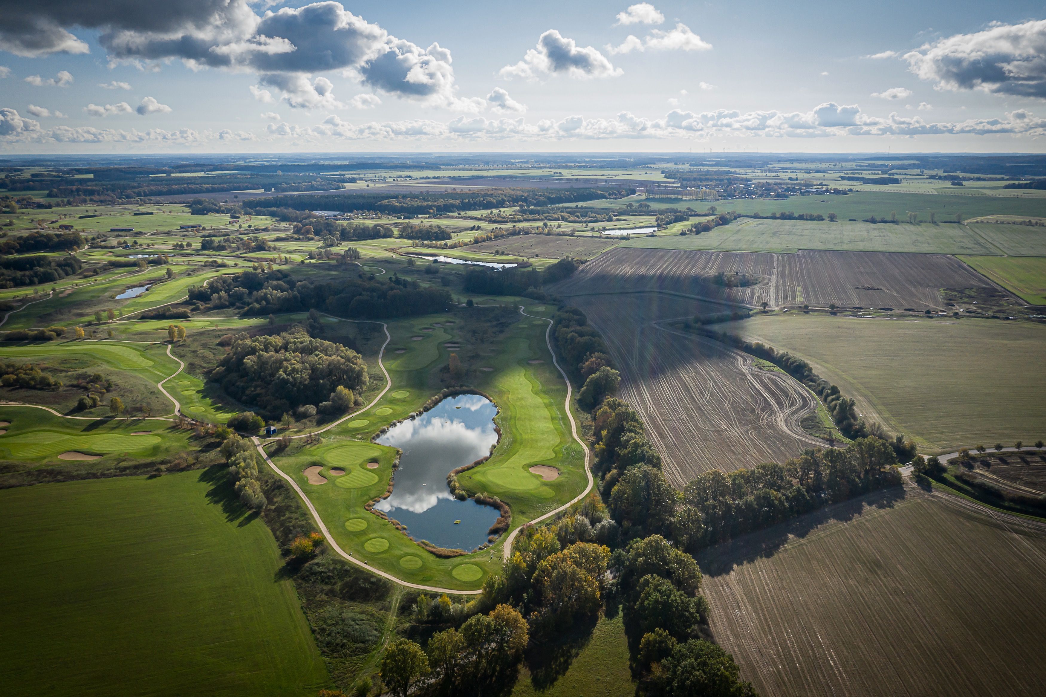 An aerial view of a golf course with multiple holes, water bodies, and surrounding fields.