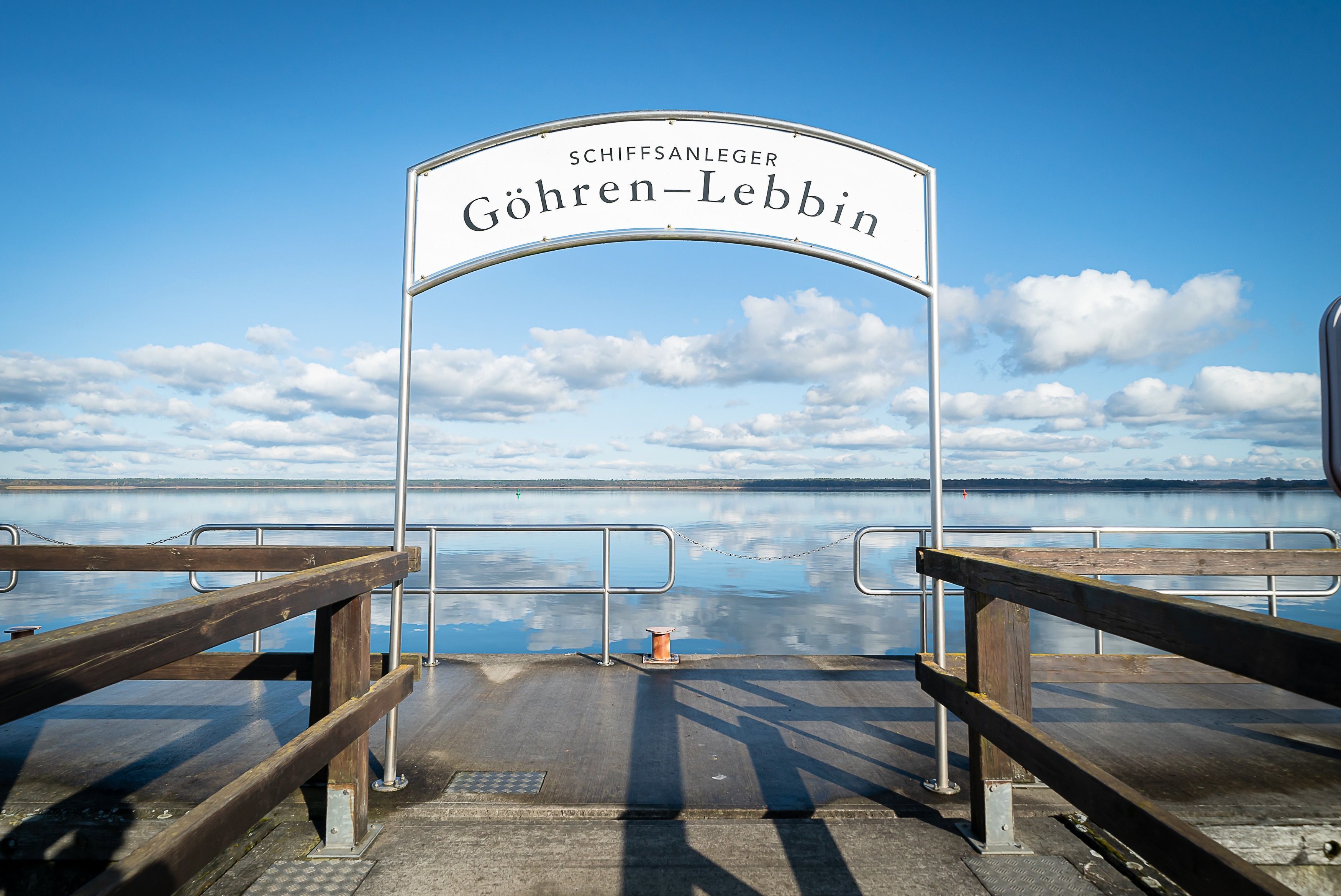 A pier with a sign reading "SCHIFFSANLEGER GÖHREN-LEBBIN" and a view of the water and sky.