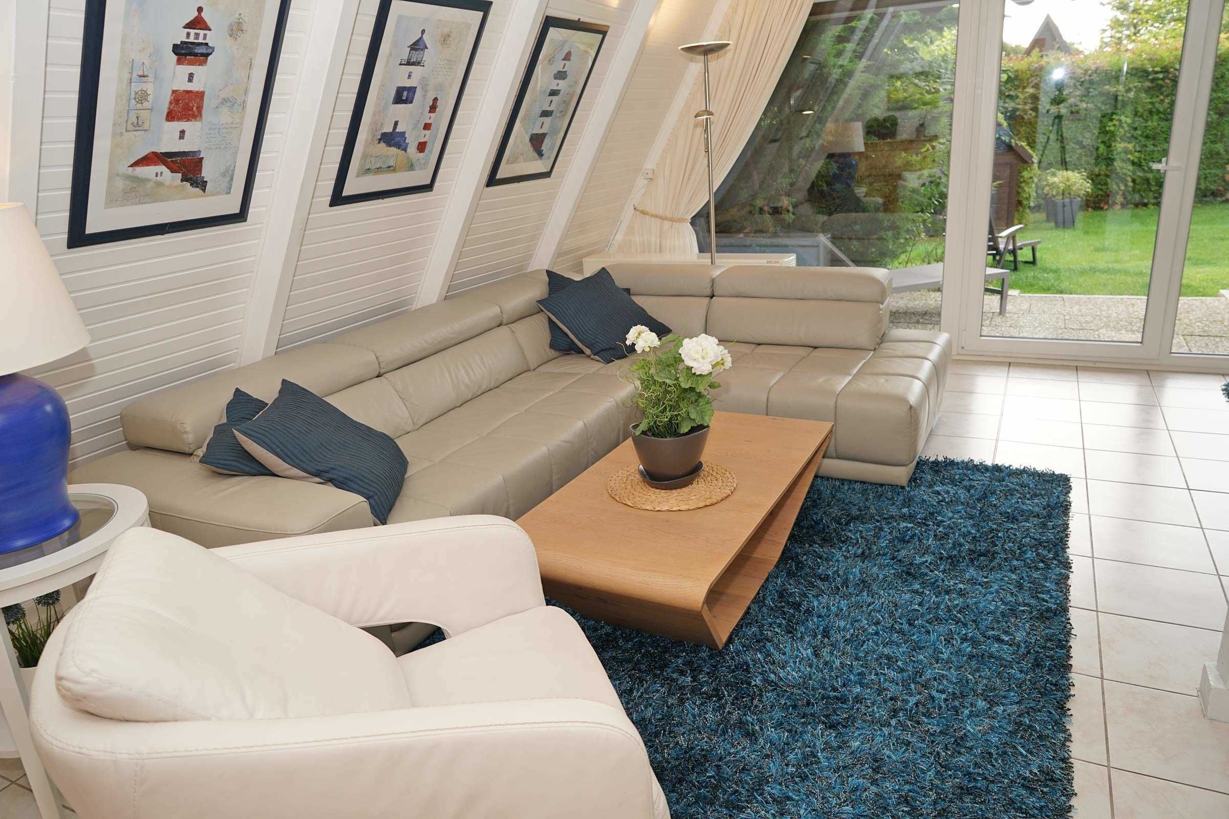 Un salón moderno con un sofá modular color crema, un sofá blanco pequeño y una mesa de centro con una planta. Hay cuadros enmarcados en la pared y un ventanal con vista a un jardín.
