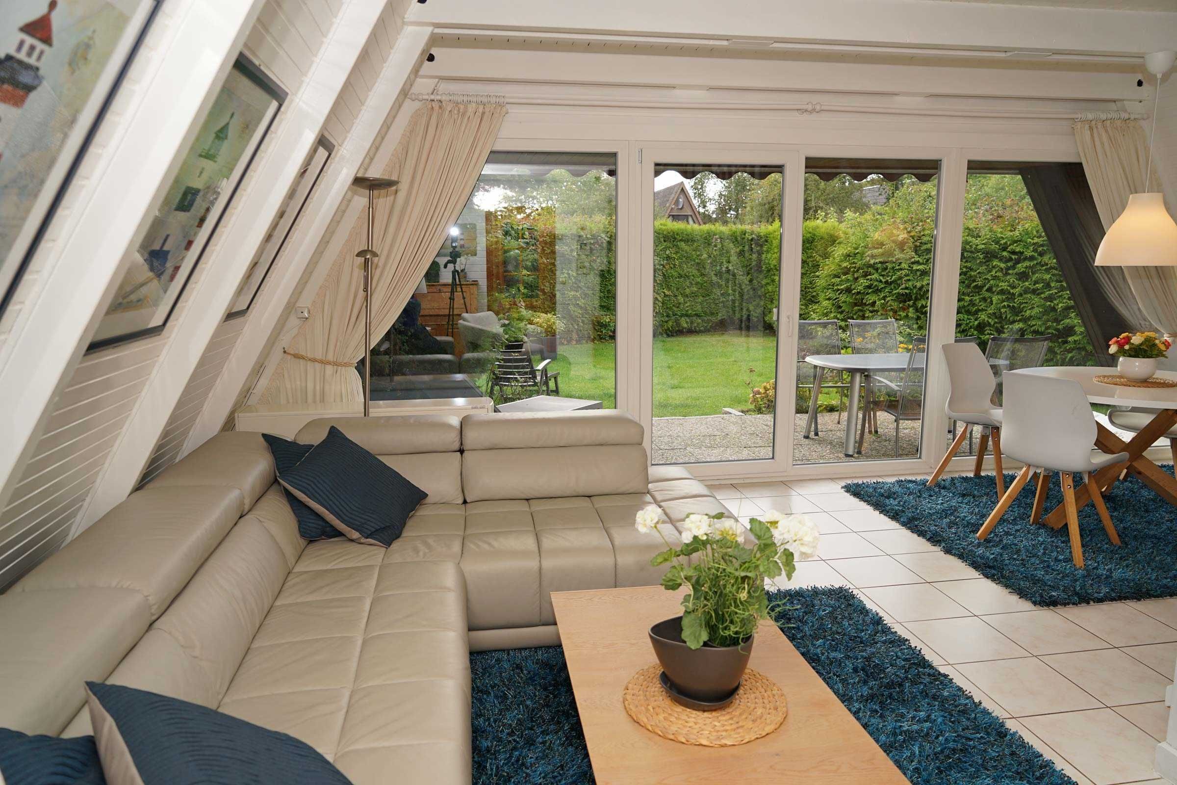 A modern living room with a beige sofa, a wooden coffee table with a plant, and a dining area with a table and chairs.
