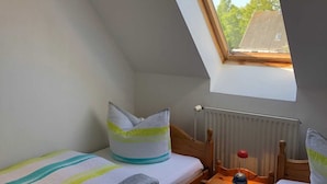 A small, cozy room with a sloped ceiling and a skylight. There are two single beds with striped bedding and pillows. A small wooden table with a red lamp is between the beds. - Villa Apartment 3 - run house en au (Fehmarn)