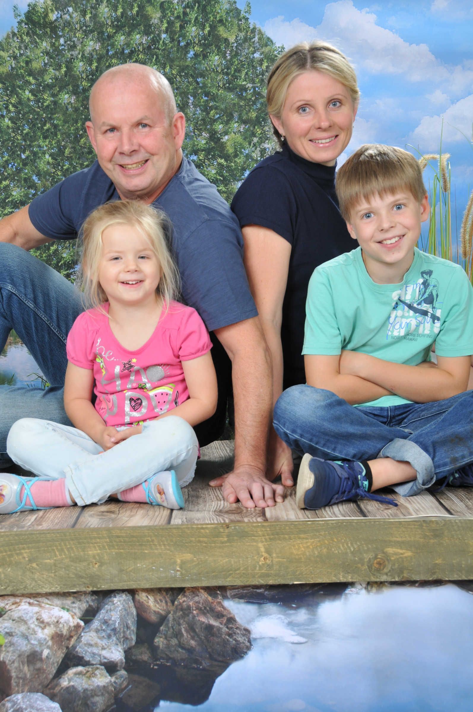 Neljän hengen perhe istuu puisen terassin reunalla, ja heidän alapuolellaan on vesiaihe.