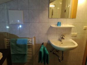 Une salle de bain équipée d’un lavabo, d’un miroir, d’un porte-serviettes et d’un espace douche.