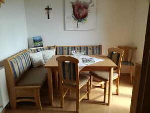 A dining area with a wooden table, four chairs, a bench with striped cushions, and a wall-mounted cross. - Apartment Edelweiss-Olgurt (Weng)