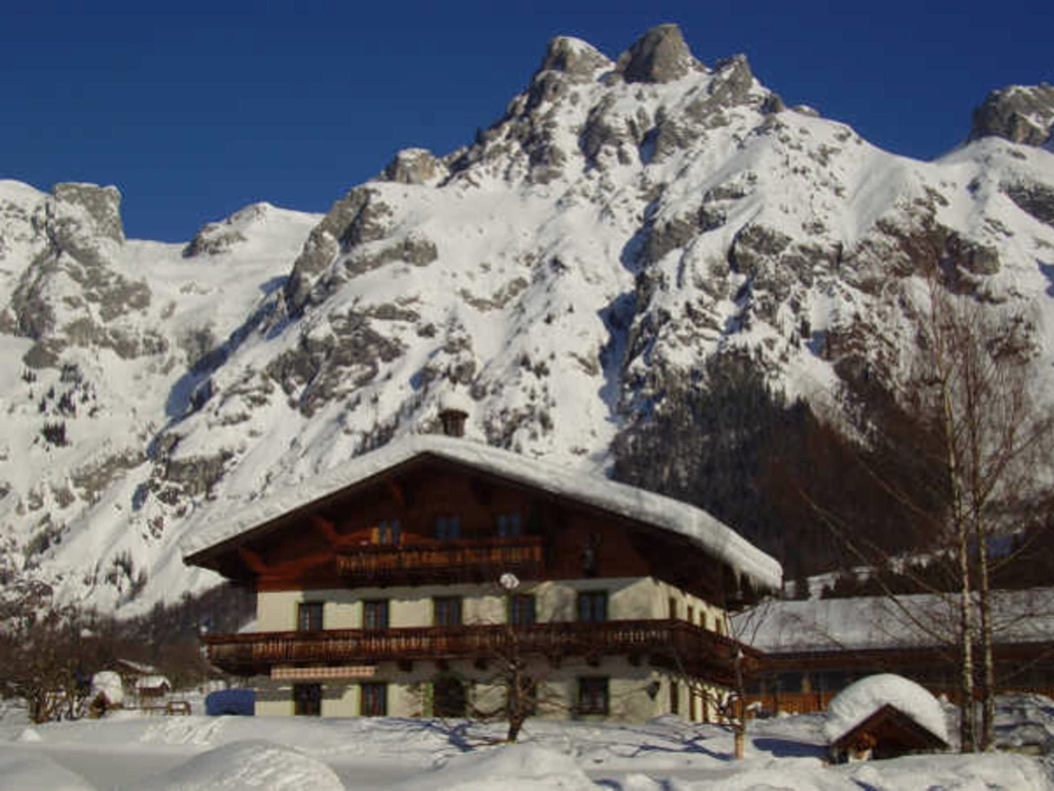A mountain lodge with a wooden structure, snow-covered surroundings, and a clear blue sky.