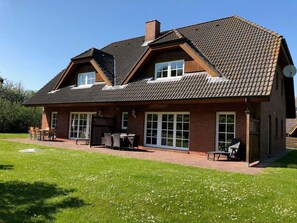 A two-story house with a sloped roof, large windows, and a patio area with outdoor furniture.