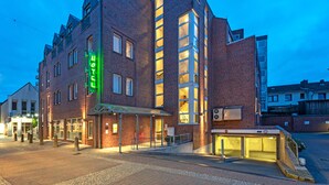 A modern hotel with a prominent neon sign, a covered entrance, and a brick facade. - Hotel DH VEC (Vechta)